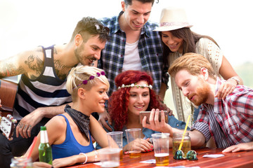 Boys and girls on picnic in nature having fun while watching photos on mobile phone