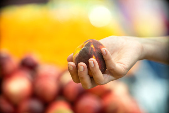 Woman's hand choosing peach in supermarket