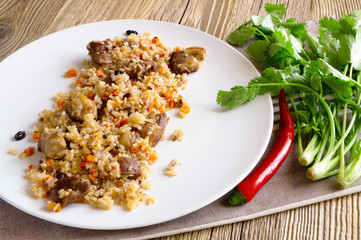 mutton pilaf served with hot pepper and fresh cilantro on wooden background