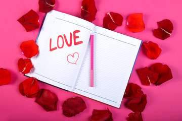 The word love written in red felt-tip pen in a notebook on a pink background in the design of rose petals.