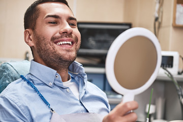 Your smile is our mission. Handsome male patient looking at his beautiful smile sitting at the...