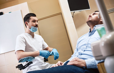 Obraz premium Dentistry with a personal touch. Dentist in mask and latex gloves sitting near his patient in dental clinic