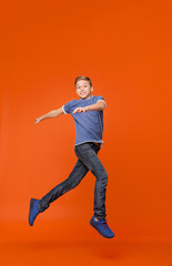 Fototapeta na wymiar Cute boy dancing, jumping in air on orange backgrouns