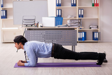 Young handsome male employee doing exercises in the office