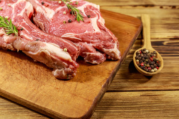 Raw fresh beef rib eye steaks on bone with spices and rosemary on wooden table