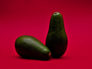 Two avocados one  standing on red background. Fresh exotic vegetables.