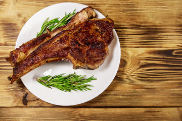 Roasted beef rib eye steak on bone with rosemary in white plate on wooden table