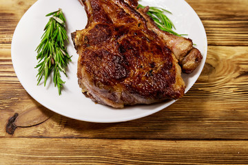 Roasted beef rib eye steak on bone with rosemary in white plate on wooden table