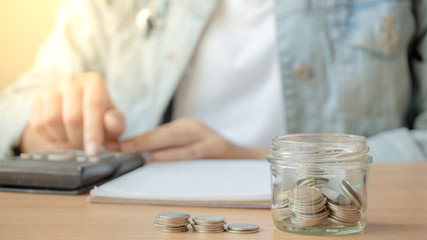 Fototapeta na wymiar Coins in glass jar saving money and female counting on calculator. 