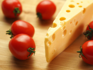 Cheese with big holes and tomatoes on a wooden table