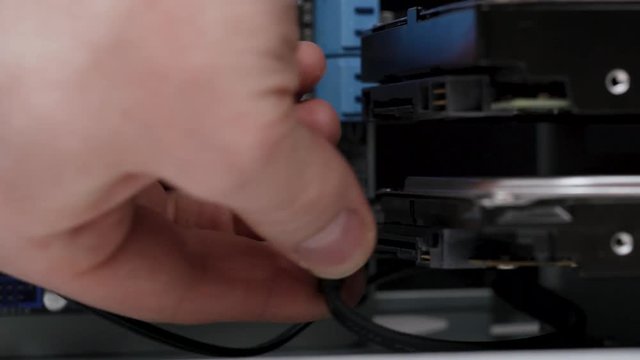 Close-up computer assembly. Male service worker connects SATA cables to hard drives inside PC case.