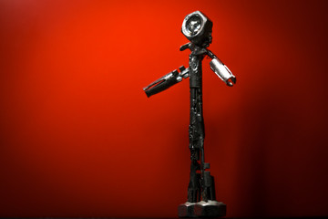 Small welded figurine of scrap metal and screw bolt as a head with wondering attitude against a red...