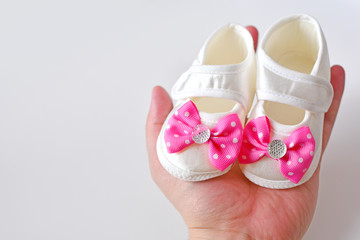 Father hand holds daughter booties with pink bow, copy space