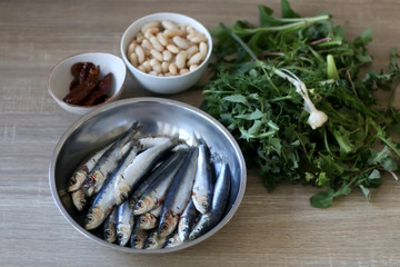 Fresh sardines, white beans, dried tomatoes and chicory on a wooden table. Ingredients for a meal. Selective focus.