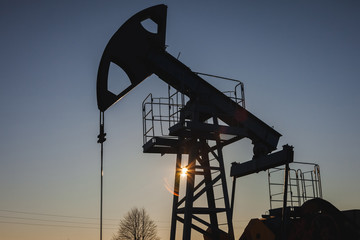 Oil pump on the background of blue sky and the morning sun, sun glare on the oil pump