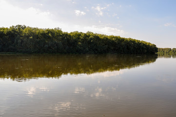 Wide yellow river is slow flowing. Early autumn. Sunny weather and brightgreen trees on the banks fron the both sides