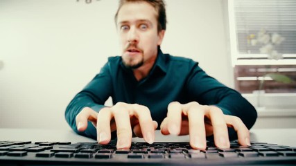 Man doing funny faces while typing on keyboard 4K. Low angle view from behind the keyboard with male person fingers in focus while typing.