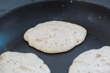 raw pancakes on black non stick pan