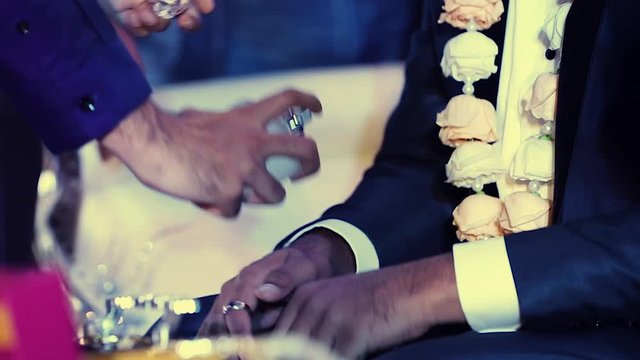 Slow motion closeup video of a man spraying perfume on a groom's wrist during a muslim wedding engagement ceremony
