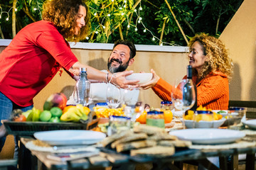 Frienship and friends at home or restaurant eating together having fun and enjoying the nightlife - table full of food and cheerful people - colors and cheerful middle age man and two women