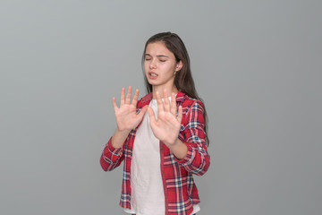 young girl put her hands in front of her, a gesture of refusal, gray wall background