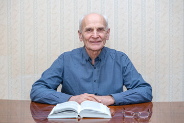 an elderly man sits at the table and smiles broadly, an open book lies on the table