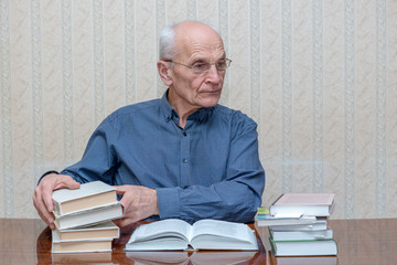an elderly man with glasses sits at a table and holds books in his hands