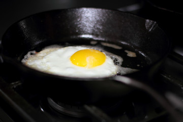 Egg sunny side up frying in a pan on the stove.