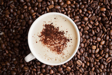 white cup with fragrant cappuccino with froth sprinkled with grated chocolate stands in coffee beans