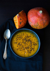 pumpkin soup in a dark plate with a spoon and pieces of pumpkin