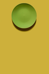 Green plate on a yellow backgroung. Deep shadow. Postcard, Design. Pace for text, copy space.