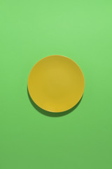 Yellow plate on a green backgroung. Deep shadow. Postcard, Design. Pace for text, copy space.