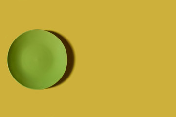 Green plate on a yellow backgroung. Deep shadow. Postcard, Design. Pace for text, copy space.