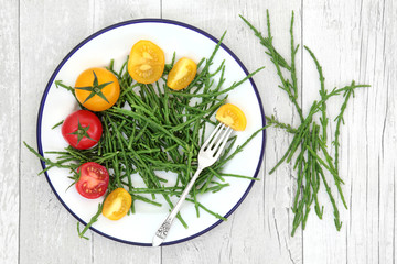 Samphire health food sea vegetable with yellow and red tomatoes on a metal plate with old silver fork, high in antioxidants, fucoidans, dietary fiber and calcium. Salicornia europaea