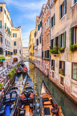 Narrow beautiful street with parked gondolas, Venice, Italy. Vertical view of old canal in summer. Vintage houses of Venice.