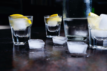 Vodka. Shots, glasses with vodka and lemon with ice .Dark stone background.