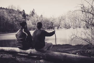 men sitting in a down tree in front of a lake in the forest