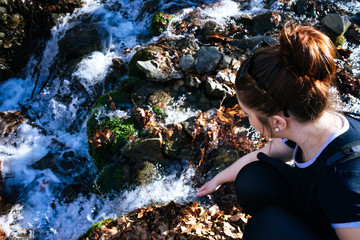 young girl hiking taking water in a stream in the forest with a stick