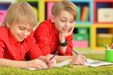 Two smiling boys in red shirts drawing with pencils