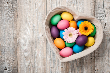 Easter eggs and gerbera flowers in heart shaped basket