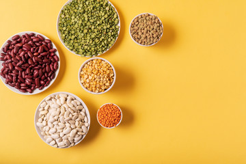 Top view of assortment of peas, lentils, beans and legumes over yellow background.