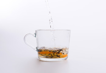 Water pouring into glass cup with tea and slices of orange isolated on white