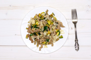 Ready to eat. recipe step by step fusilli pasta with zucchini on white porcelain plate with a fork flatlay on white wood