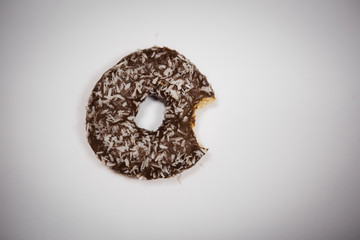 A bitten donut lies on a white background. A piece of half-eaten chocolate doughnut with coconut.