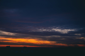 Cityscape with wonderful varicolored fiery dawn. Amazing dramatic multicolored cloudy sky. Dark silhouettes of city building roofs. Atmospheric background of sunrise in overcast weather. Copy space.
