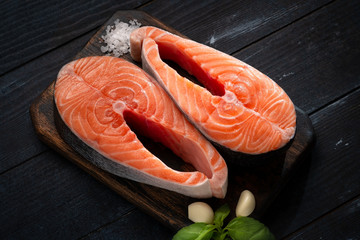 Two Raw Salmon steak on a wooden Board with salt and basil on a dark background. Fresh red fish....