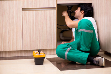 Young plumber repairing wash basin at kitchen