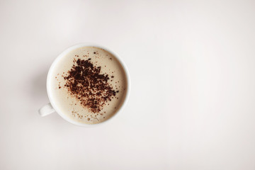  white cup with cappuccino and frothy and grated chocolate on a beige background and free space for the inscription on the right