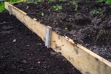 Garden bed fenced with wooden plank, in the countryside garden, on a spring day. Soil preparation for planting vegetables.