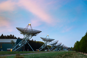 The Westerbork Synthesis Radio Telescope (WSRT) during dusk, with a light cloudy sky and stars a...